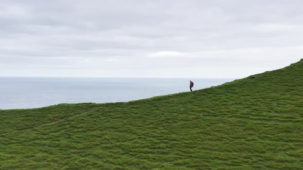 Aerial View of Unrecognizable Woman Walking in a Dirty Road in a Green Mountain Ridge with Backpack