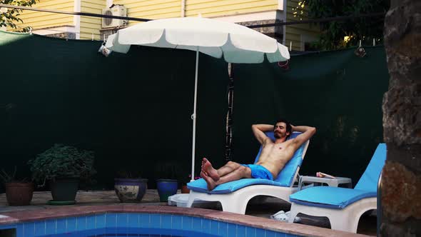 Footage of Bearded Caucasian Man Lying on Sunbed in Front of Swimming Pool with Hands Behind Head