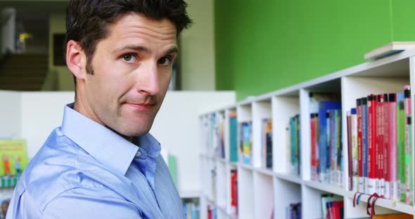 School teacher taking a book from bookshelf in library at school