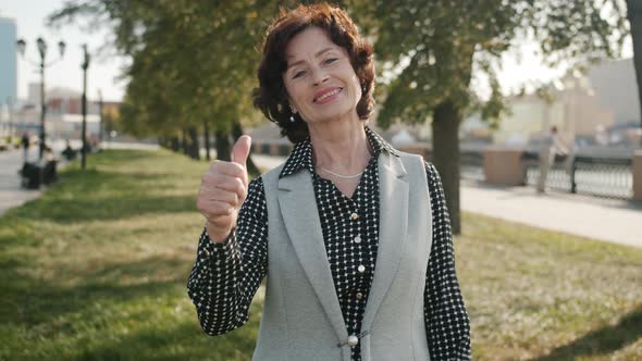 Portrait of Happy Senior Woman Smiling and Stretching Arms with Thumbsup Hand Gesture Outdoors