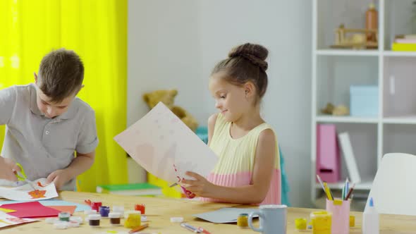 Little Boy and Girl Cutting Out Painting in Art Class alt