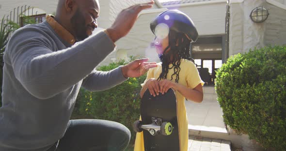 Happy african american father giving high five to daughter holding skateboard