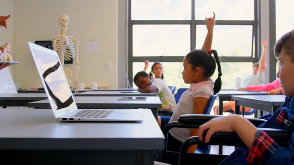 Schoolkids raising hand while sitting at desk in elementary school 4k