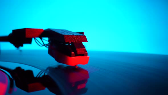 Black Vinyl Record Spinning and Play Music on Old Turntable in Rays of Bright Red and Blue Neon