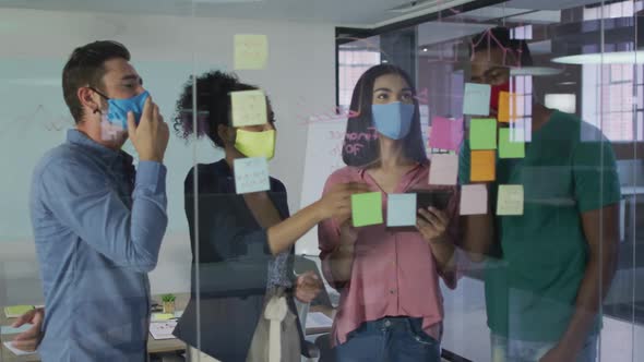 Diverse colleagues wearing face masks using memo notes on glass wall having a discussion