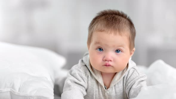 Portrait of Pretty Innocence Little Baby with Blue Eyes Posing at White Bedroom Interior