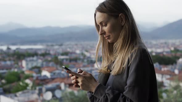 Woman Using a Smartphone While Standing on Top View Point of the City