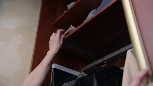 girl opens the cabinet door and hides a small stack of money on the top shelf