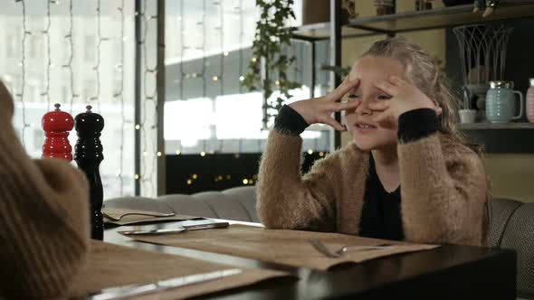 a Girl Closes Her Eyes Sitting in a Restaurant with Her Mother