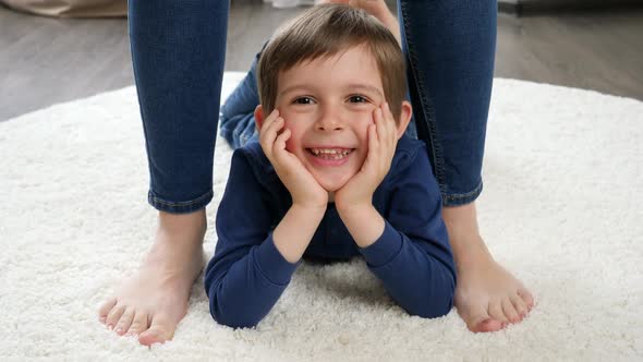 Portrait of Happy Smiling Little Boy Lying on Carpet Between Mother's Feet