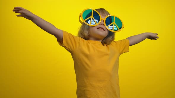 Cute Little Girl in Yellow Hippie Sunglasses is Dancing on the Yellow Background