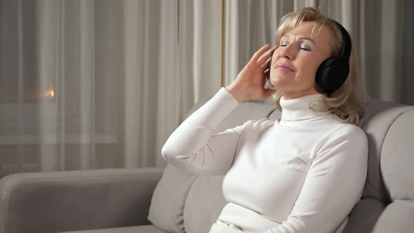 Blonde Woman of Middle Age Listens to Music Via Headphones