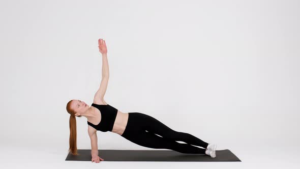 Athletic Young Woman Doing Side Plank Rotations Exercise While Training In Studio