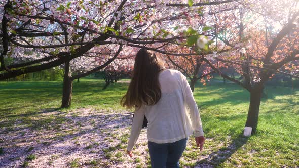 Young woman with long hair enjoys spring garden in bloom. Girl walking in Japanese Garden