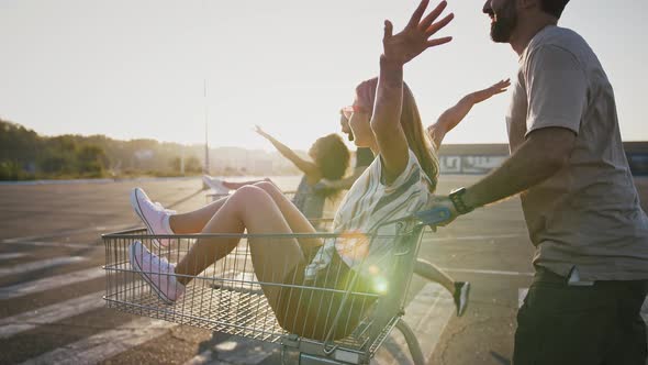 Friends Racing on Shopping Trolleys with Their Girlfriends at Deserted Car Parking