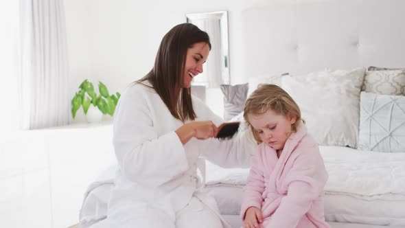 Caucasian mother and daughter having fun brushing hair in bedroom