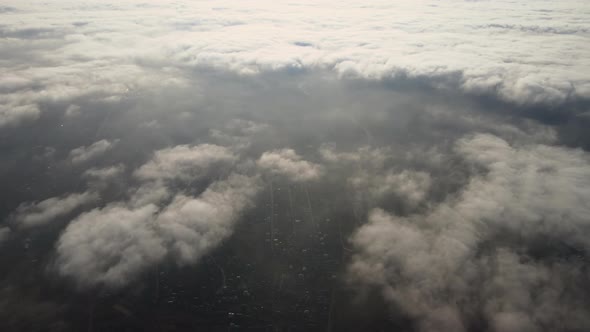 Aerial View From High Altitude of Distant City Covered with Puffy Cumulus Clouds Flying By Before