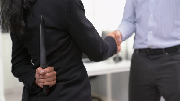 Back View of Businesswoman Shaking Hands with a Knife Behind His Back