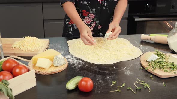 Hands putting blue cheese on pizza base