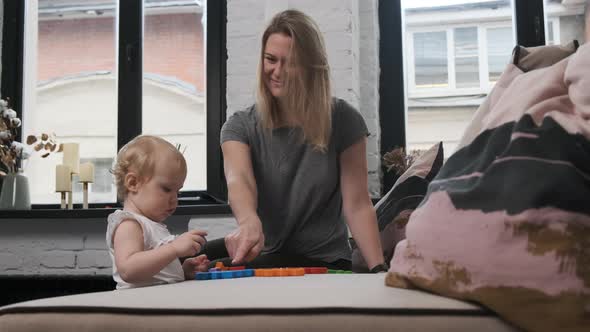 Mom and Cute Little Daughter Child in White Clothes Are Playing on the Bed in Colored Cubes. The