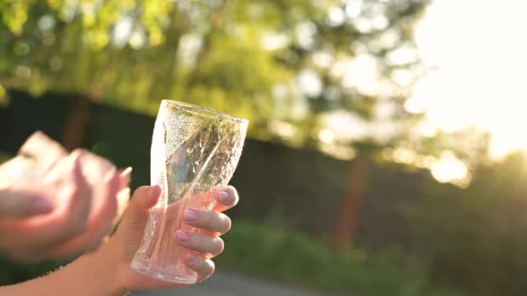 Young woman throws ice cubes into a glass glass on a hot evening to pour a drink