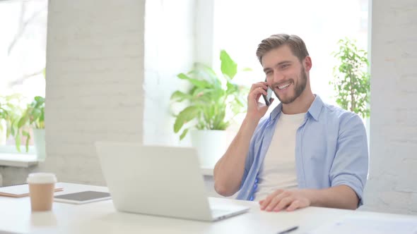 Young Creative Man with Laptop Talking on Smartphone