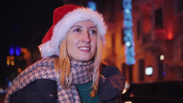 a woman chatting on her smartphone wearing a Santa hat is a night city.