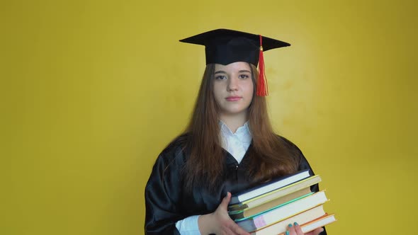 Caucasian Young Girl Student Holds Many Books While Staying in Front of Camera on Yellow Background