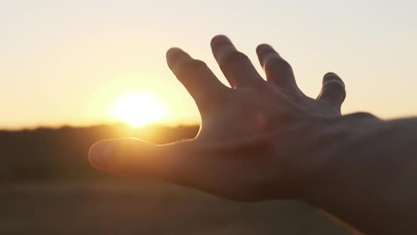 Male Hand Against Sunset. Touch the Sun. Sun Shines Through Fingers. Slow Motion