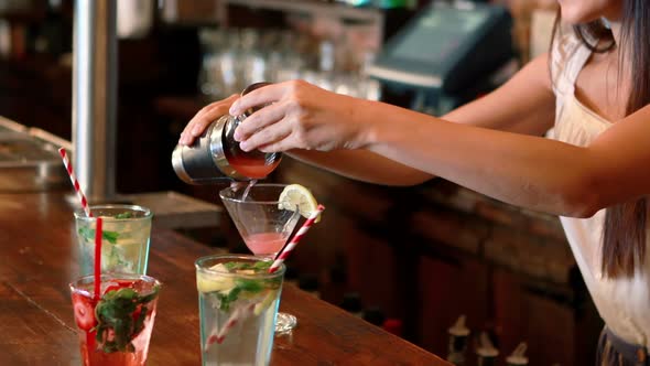 Barmaid pouring cocktail in glass at bar counter