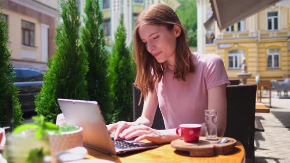 Young Woman Using Laptop in a Cafe on a Summer Terrace