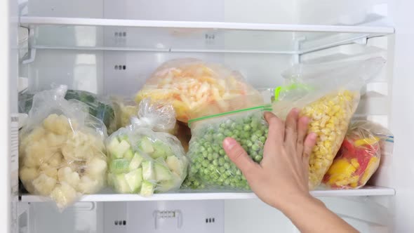 Female Hands take out bags of frozen vegetables in the fridge. Frozen vegetables