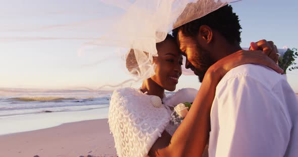 African american couple in love getting married, smiling and looking at other on the beach at sunset