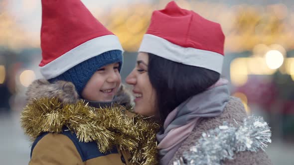 Closeup Happy Middle Eastern Mother and Son in Christmas Hats Rubbing Noses Turning Looking at