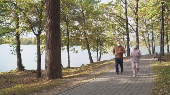 Wellness Adult Couple in Medical Masks Running Around a Forest Park Autumn Day Gray haired Man