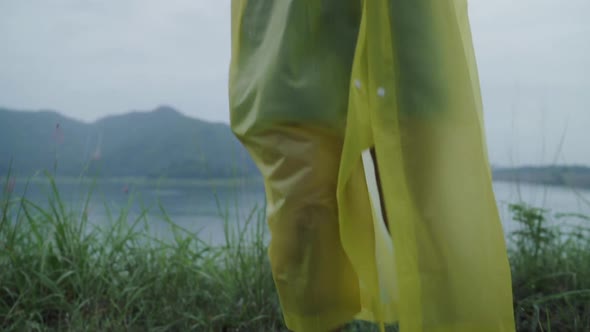 Young Asian woman feeling happy playing rain while wearing raincoat standing near lake.