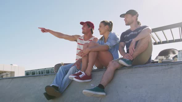 Caucasian woman and two male friends sitting talking and pointing something in distance on sunny day