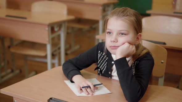 Pensive Little Girl Thinks in a School Class