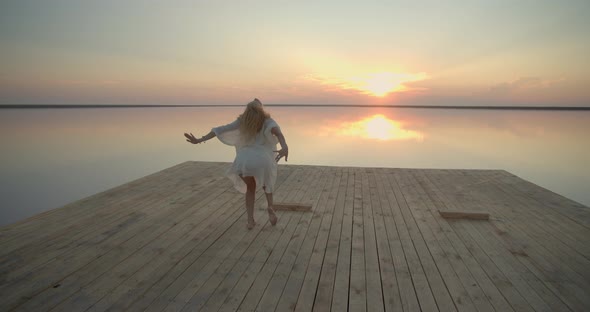 Beautiful Model is Dancing on the Lake Pier with the Amazing Sunset Behind Her