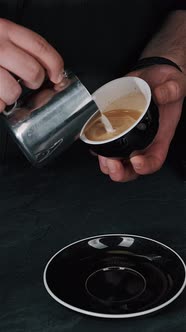 Barista pouring milk in hot coffee and making cappuccino foam in cafe close up, vertical