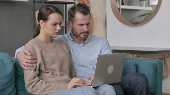 Couple Reacting to Loss on Laptop While Sitting on Sofa