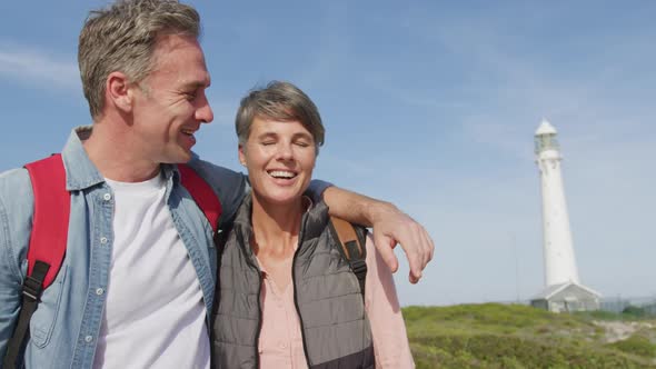 Caucasian couple enjoying free time by sea on sunny day wearing backpacks