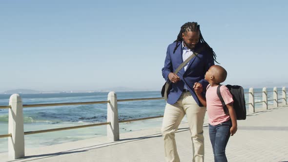 Video of happy african american father and son walking and talking by sea