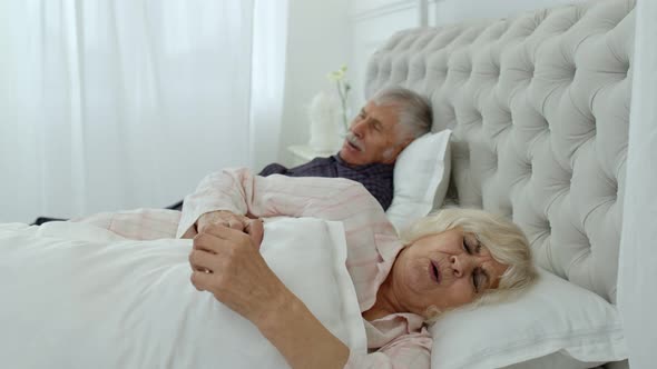 Senior Grandparents Couple Lying and Sleeping in Bed. Woman Getting Disturbed with Man Snoring