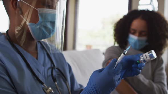 African american female doctor wearing face mask preparing covid vaccine for patient