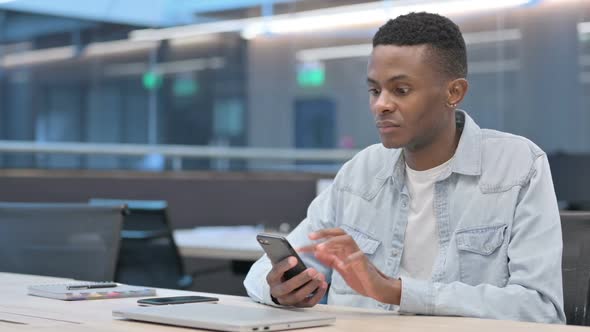African Man Reacting to Loss on Smartphone in Office