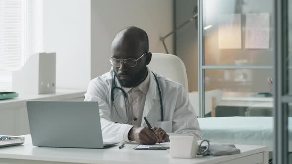 Black Doctor Working on Laptop and Taking Notes