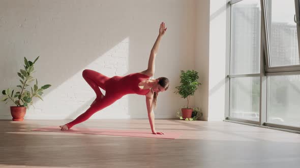 Young Woman in Red Sports Uniform Does Vasisthasana in Yoga Studio