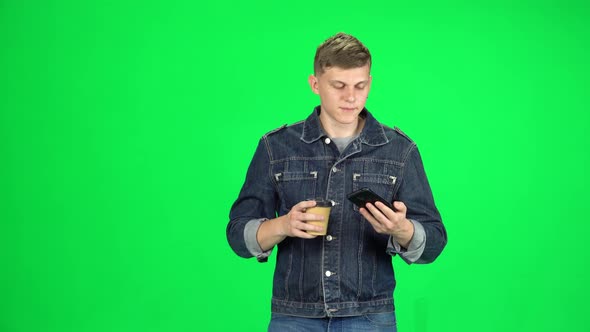 Smiling Man Goes, Takes a Selfie with Smartphone and Drinking Coffee on Green Screen at Studio
