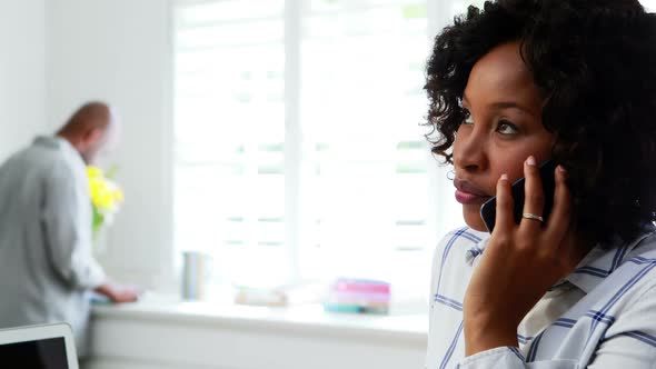 Woman talking on mobile phone while man reading a book in background